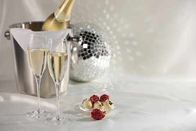 Photo of Champagne in glasses, ice bucket with bottle and tasty candies on white fabric, space for text