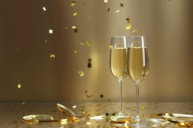 Photo of Champagne in glasses and flying confetti on golden background, space for text