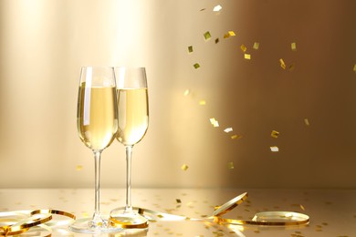 Photo of Champagne in glasses and flying confetti on golden background, space for text