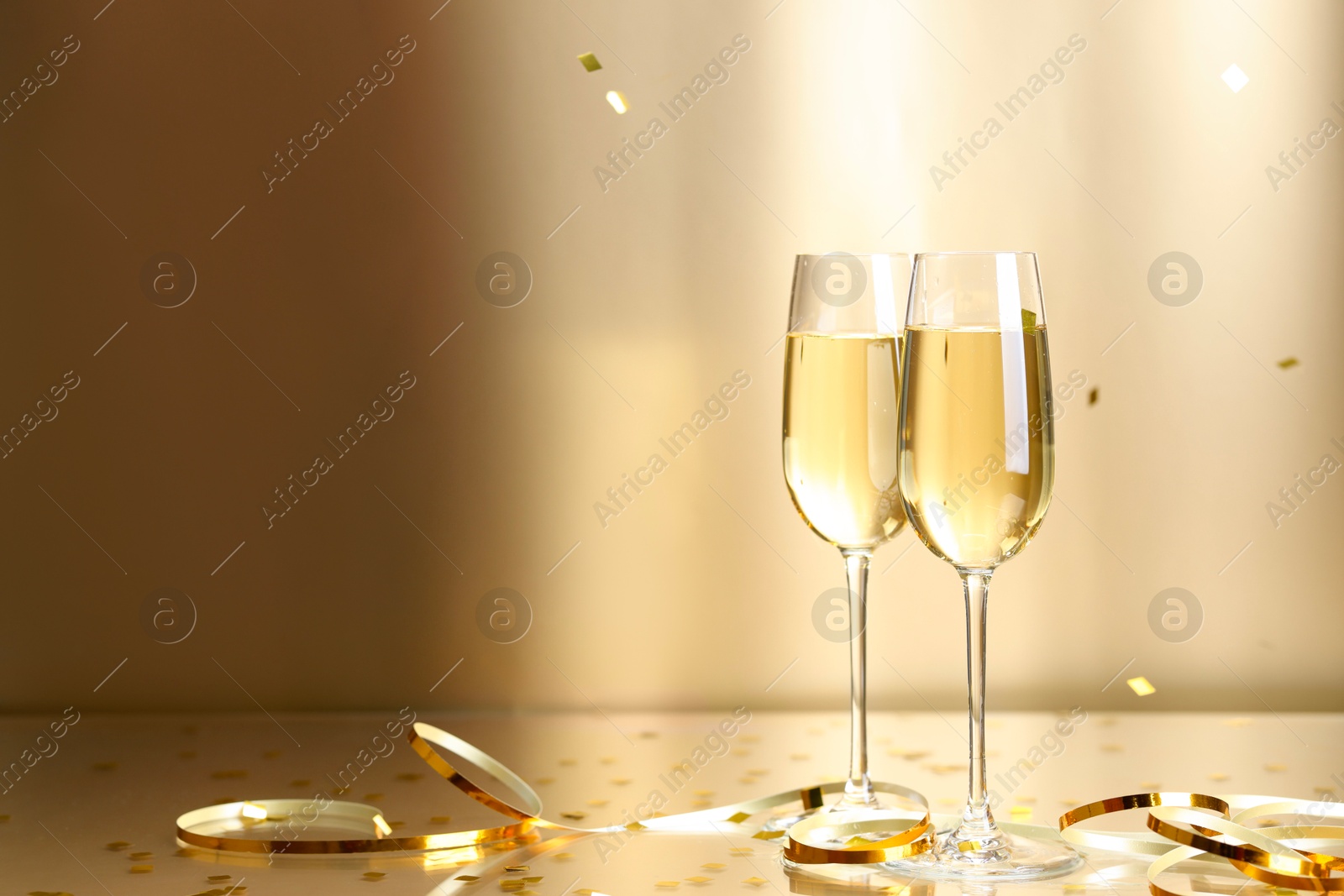 Photo of Champagne in glasses and flying confetti on golden background, space for text