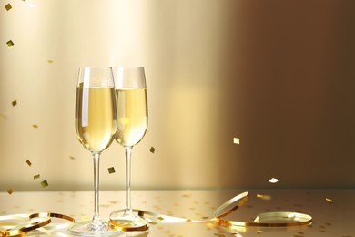 Photo of Champagne in glasses and flying confetti on golden background, space for text