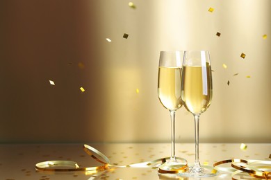 Photo of Champagne in glasses and flying confetti on golden background, space for text