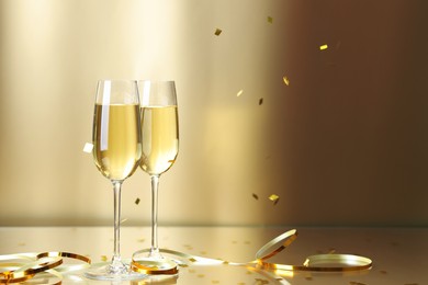 Photo of Champagne in glasses and flying confetti on golden background, space for text