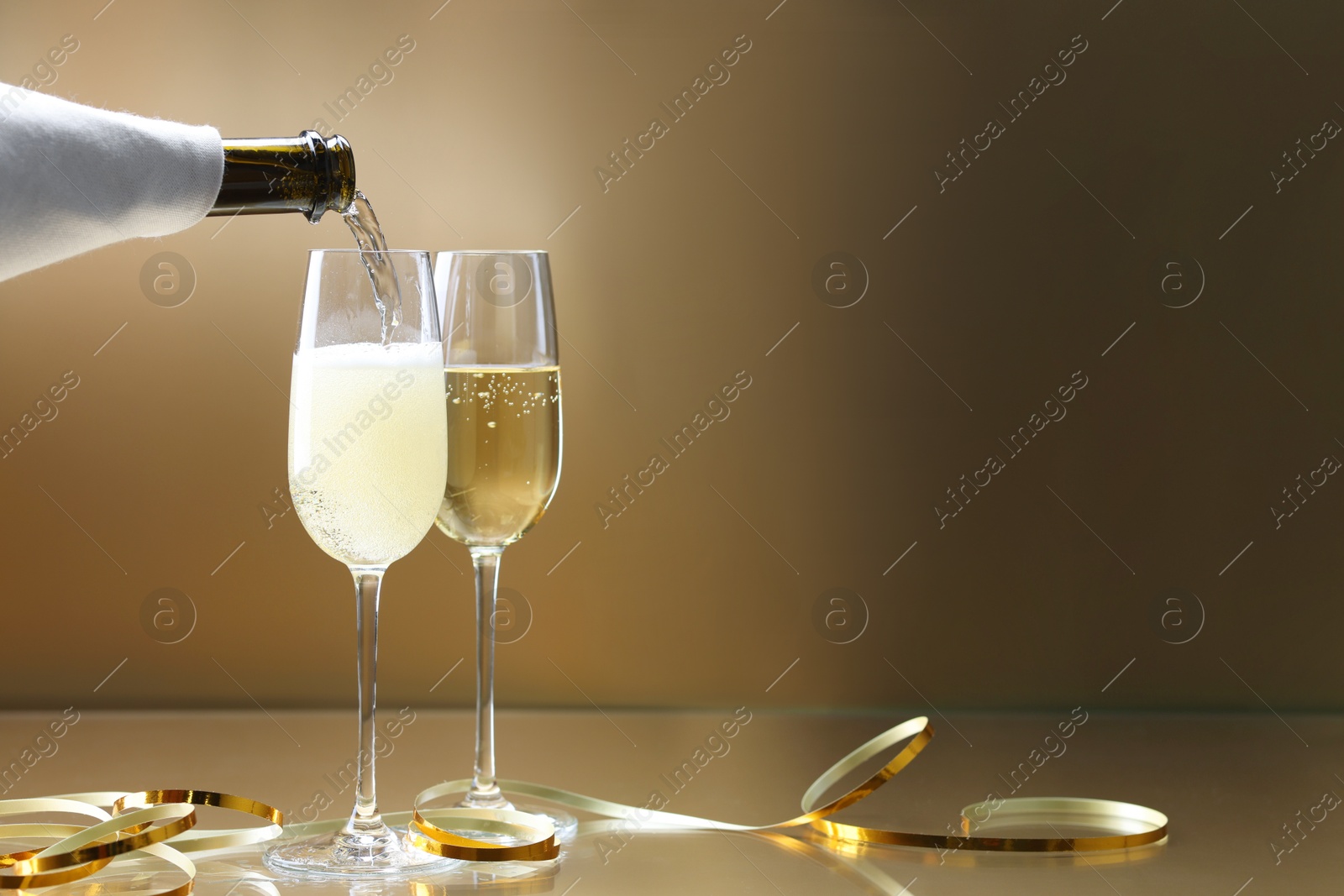 Photo of Pouring champagne into glass against golden background, closeup. Space for text