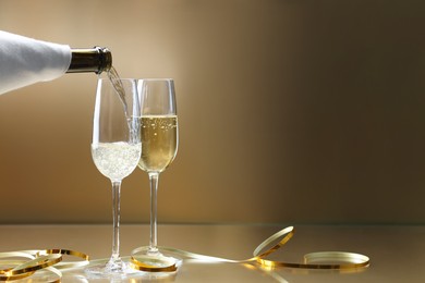 Photo of Pouring champagne into glass against golden background, closeup. Space for text