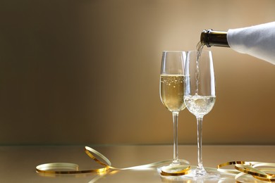 Photo of Pouring champagne into glass against golden background, closeup. Space for text