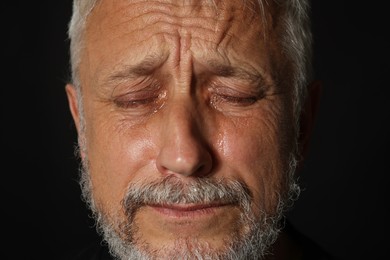 Photo of Sad senior man crying on black background, closeup