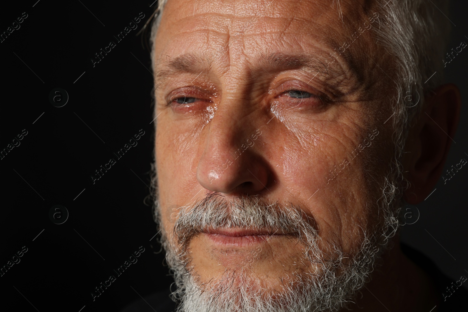 Photo of Sad senior man crying on black background, closeup