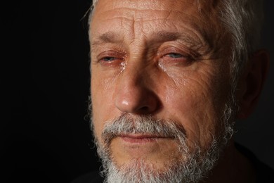 Photo of Sad senior man crying on black background, closeup