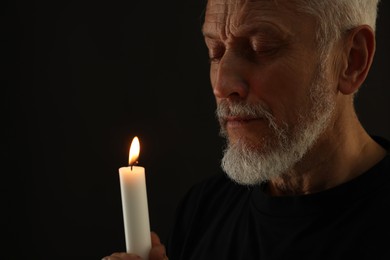 Photo of Sad senior man with burning candle crying on black background, space for text. Grieving loss