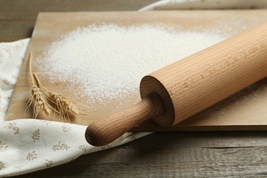 Photo of Rolling pin, board, flour and spikes on wooden table, closeup