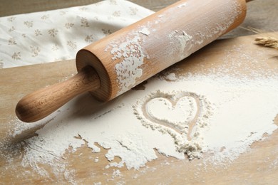 Photo of Rolling pin and heart shape made of flour on table, closeup