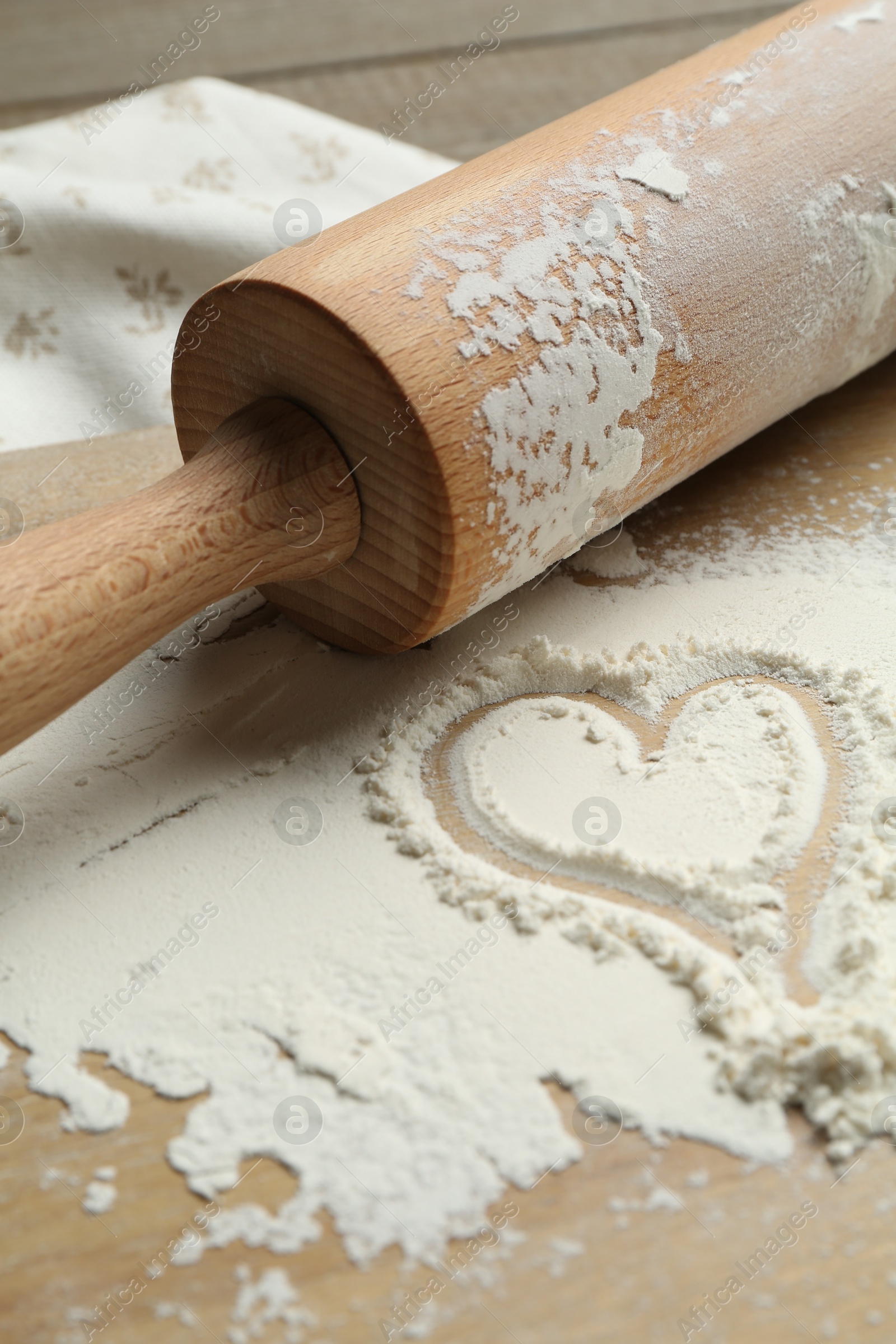 Photo of Rolling pin and heart shape made of flour on table, closeup