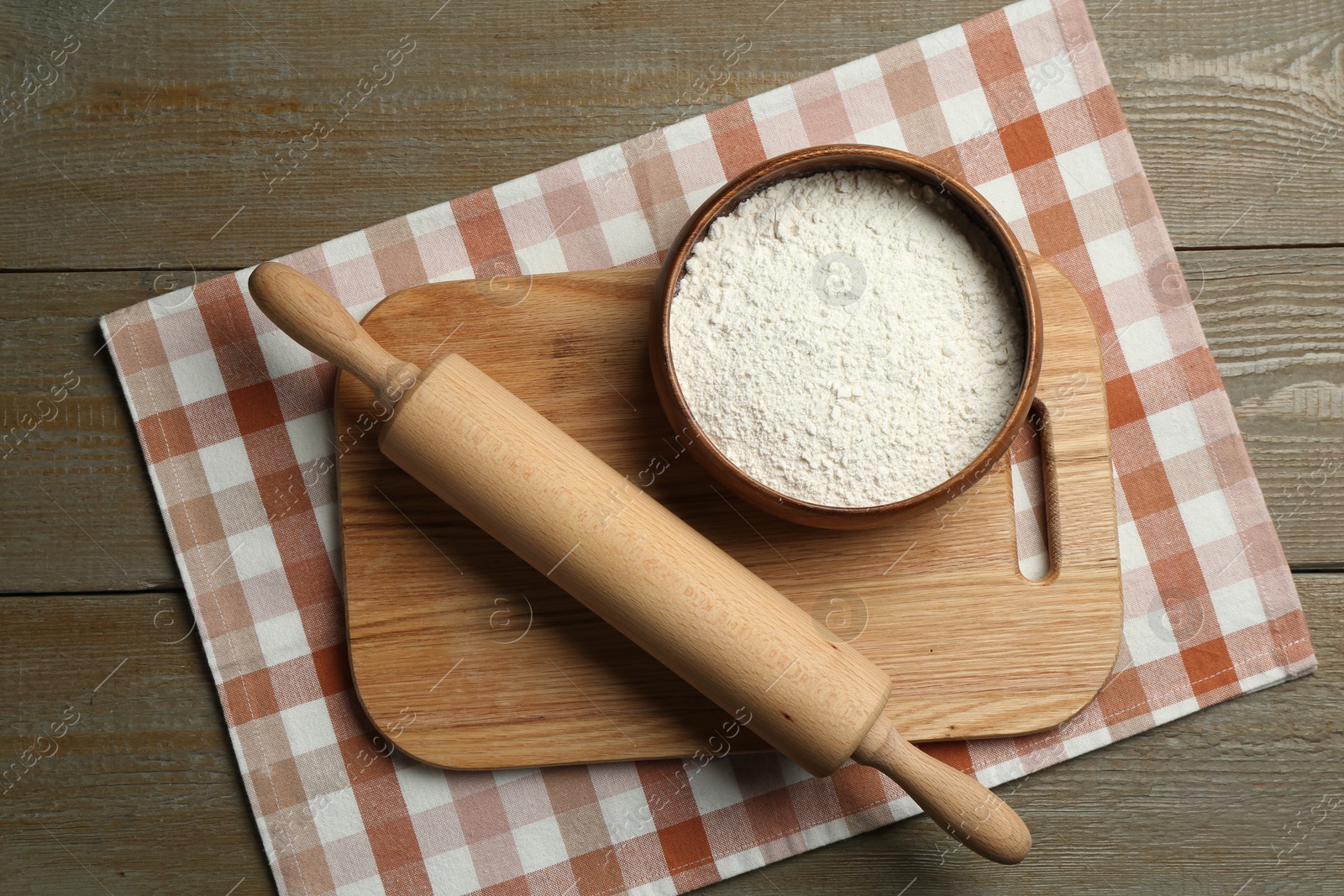 Photo of Rolling pin, bowl of flour and board on wooden table, top view