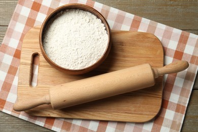 Photo of Rolling pin, bowl of flour and board on wooden table, top view