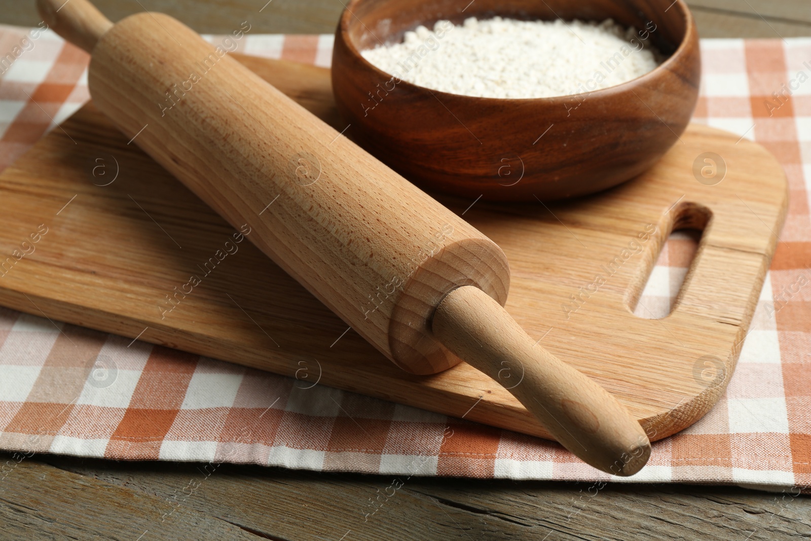 Photo of Rolling pin, bowl of flour and board on wooden table, closeup