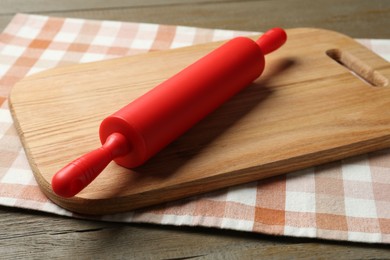 Photo of Red rolling pin and board on wooden table, closeup