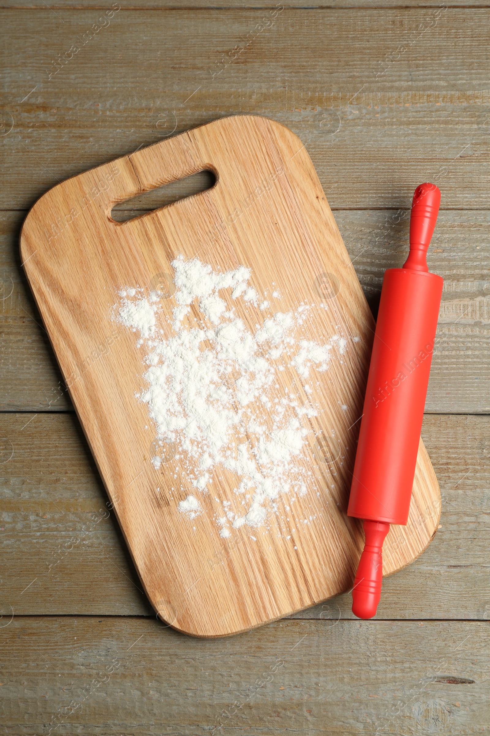 Photo of Red rolling pin and board with flour on wooden table, top view