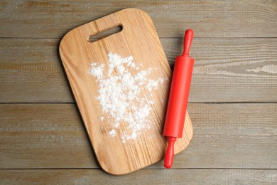 Photo of Red rolling pin and board with flour on wooden table, top view