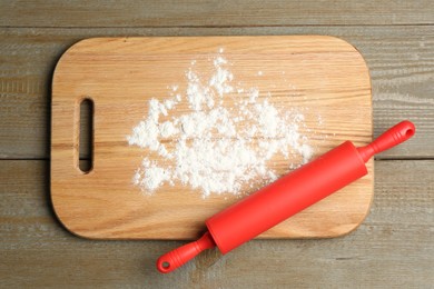 Photo of Red rolling pin and board with flour on wooden table, top view