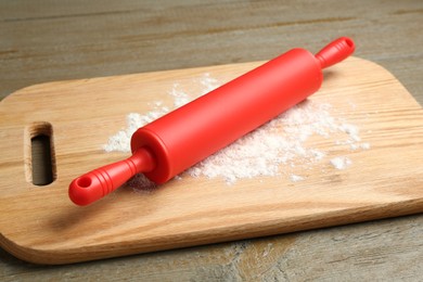 Photo of Red rolling pin and board with flour on wooden table, closeup