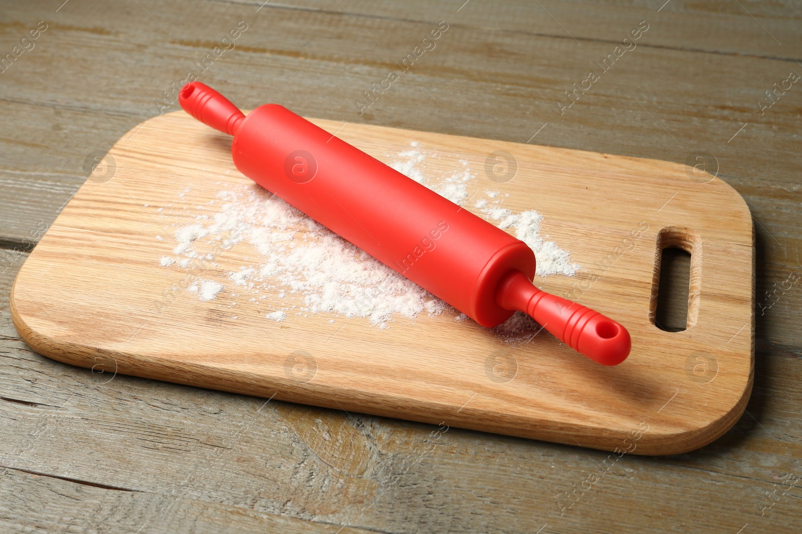 Photo of Red rolling pin and board with flour on wooden table, closeup