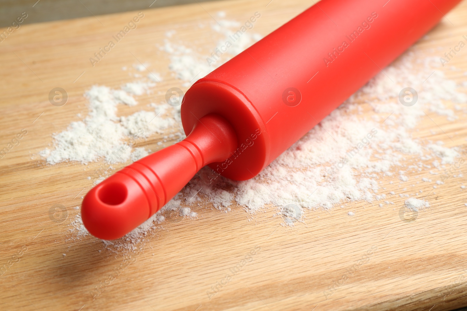 Photo of Red rolling pin and flour on wooden board, closeup