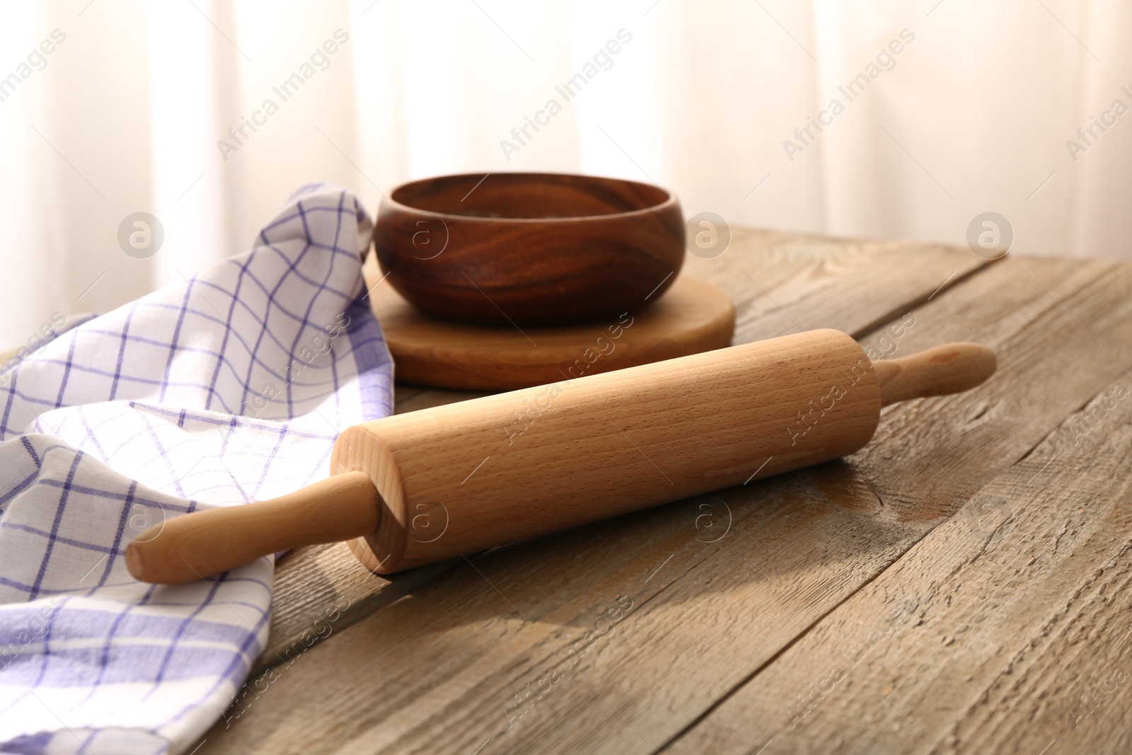 Photo of Rolling pin, napkin and bowl on wooden table indoors