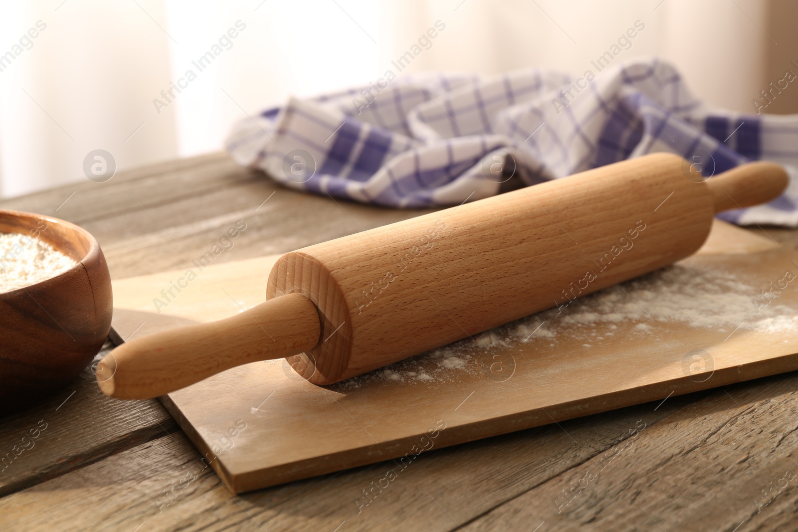 Photo of Rolling pin, flour, board and napkin on wooden table indoors, closeup