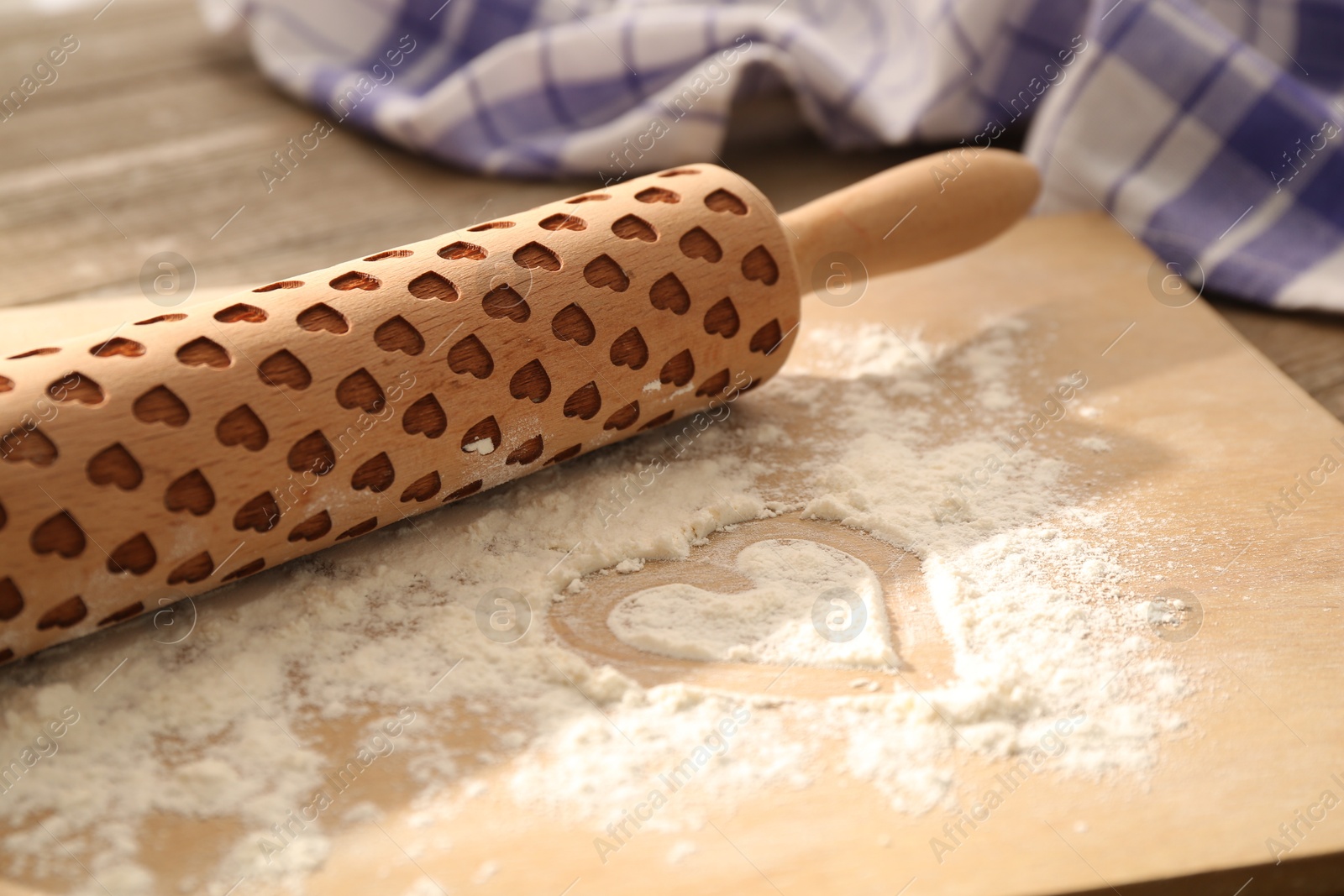 Photo of Rolling pin and heart shape made of flour on table, closeup