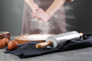 Photo of Woman with flour and rolling pin at grey table, closeup