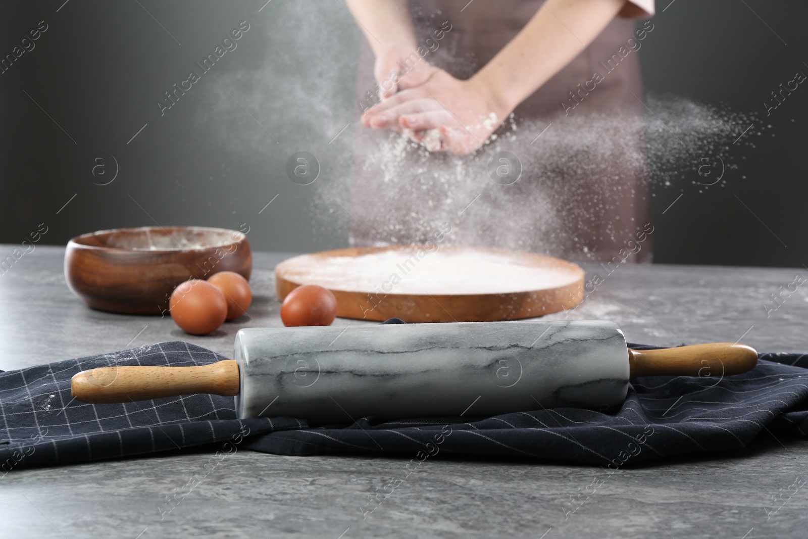 Photo of Woman with flour and rolling pin at grey table, closeup