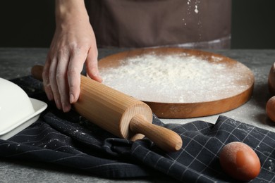 Photo of Woman with rolling pin and flour at grey table, closeup