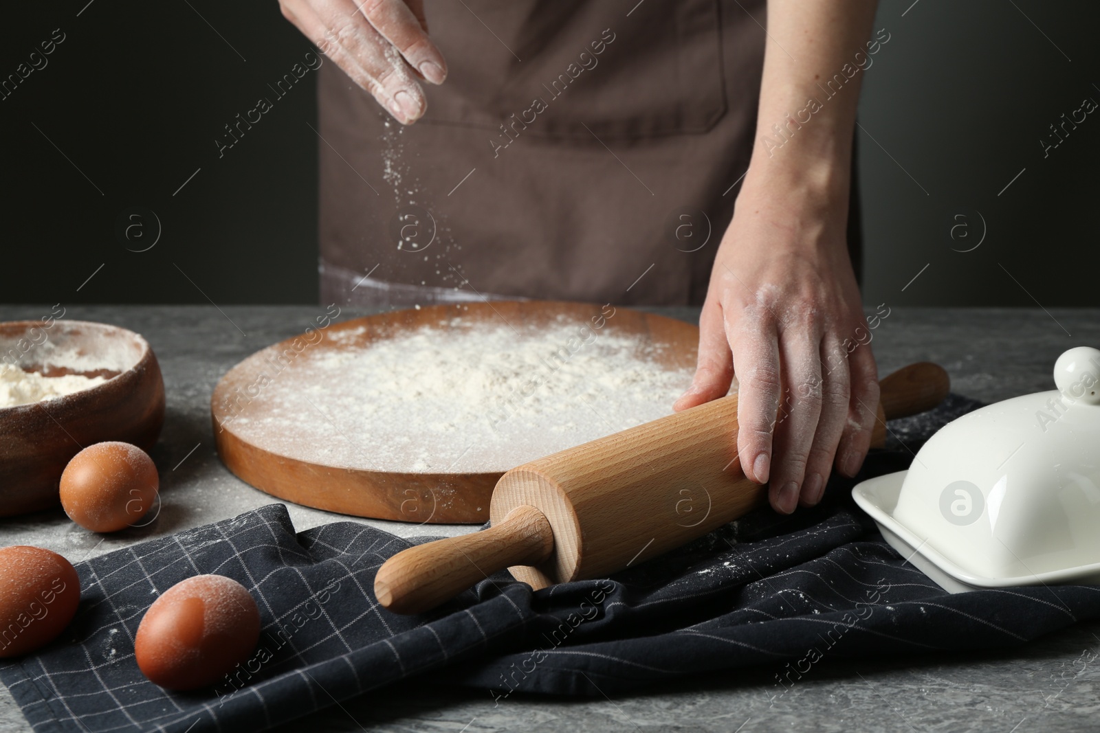 Photo of Woman with rolling pin and flour at grey table, closeup