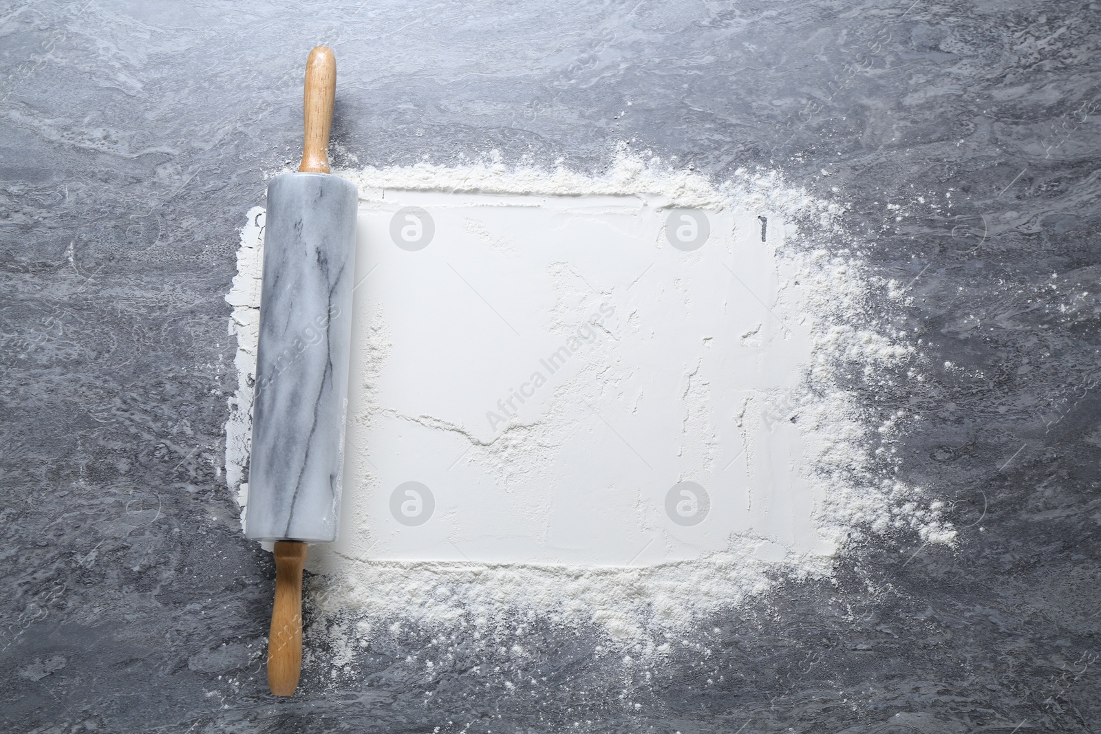 Photo of Rolling pin and flour on grey textured table, top view