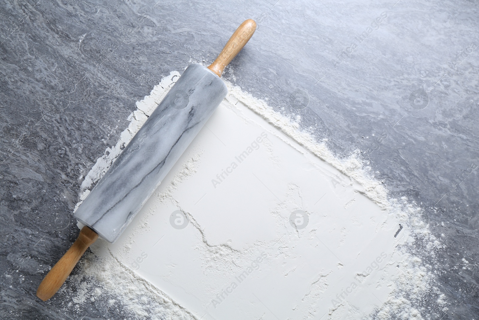 Photo of Rolling pin and flour on grey textured table, top view