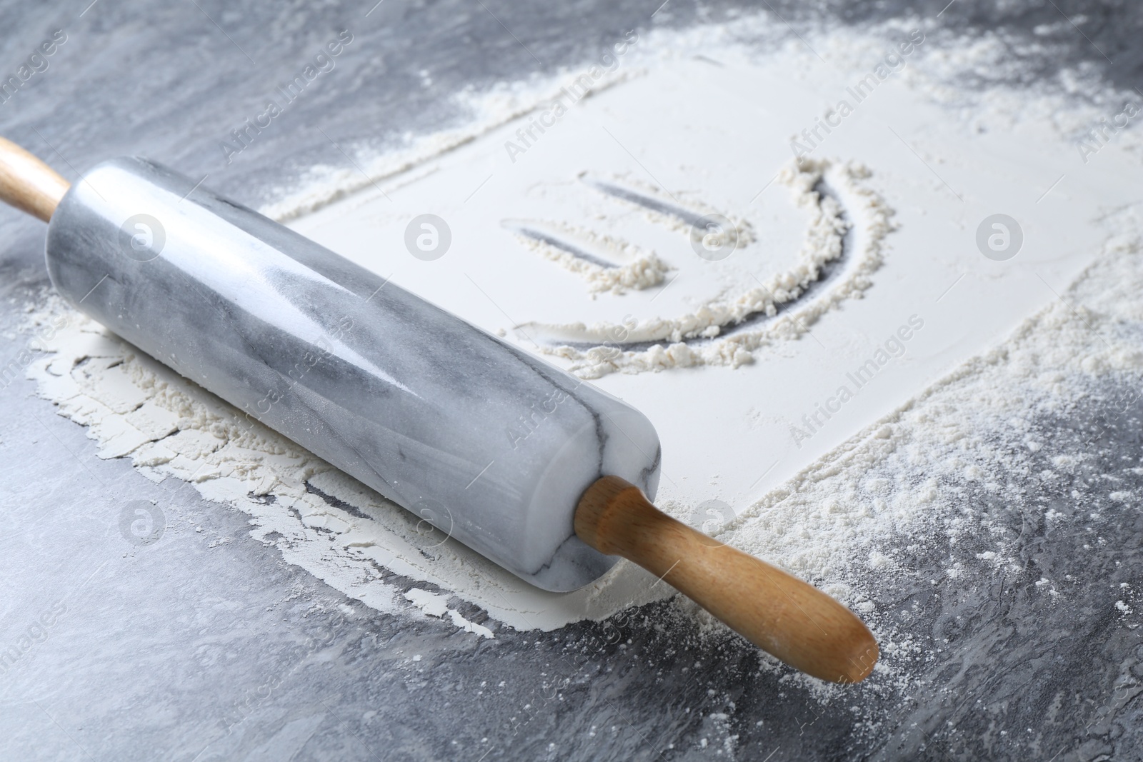 Photo of Rolling pin and smiling face made of flour on grey textured table, closeup