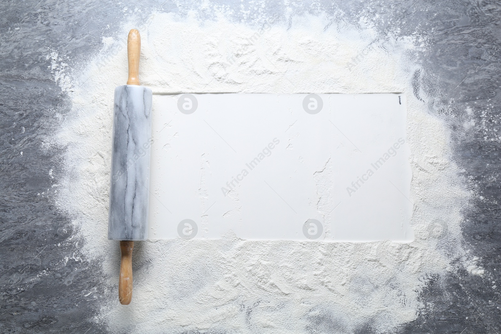 Photo of Rolling pin and flour on grey textured table, top view