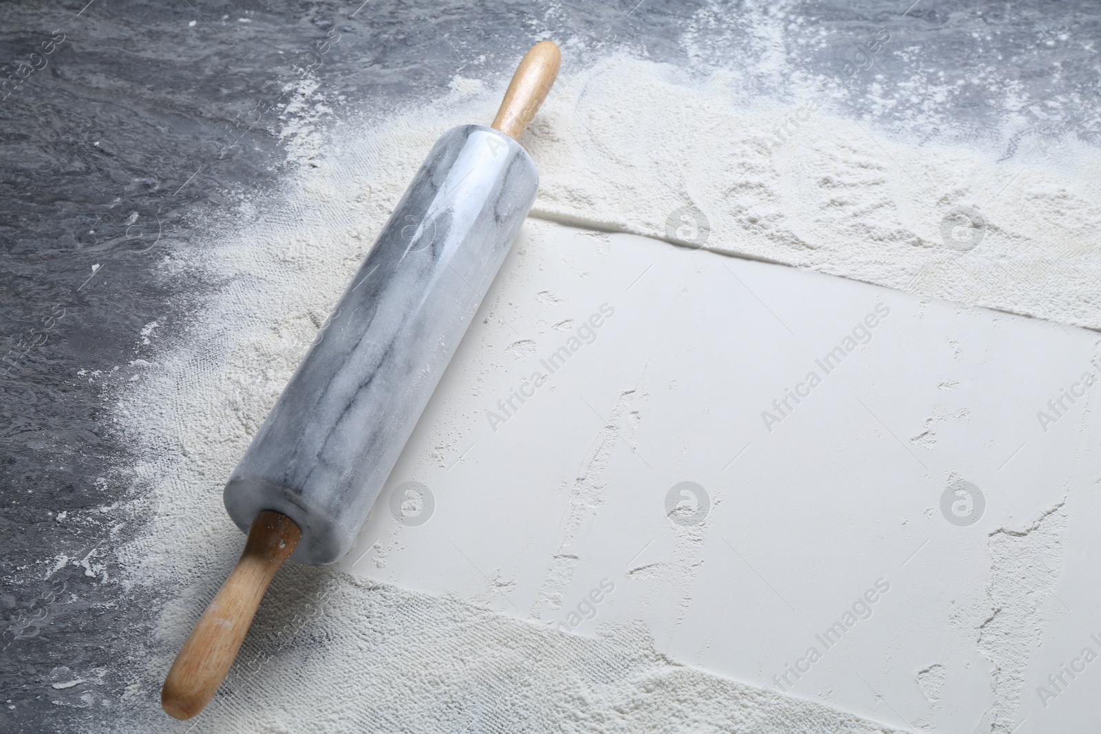 Photo of Rolling pin and flour on grey textured table, closeup