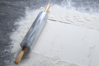 Photo of Rolling pin and flour on grey textured table, closeup