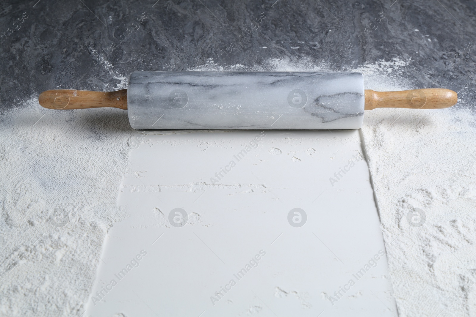 Photo of Rolling pin and flour on grey textured table