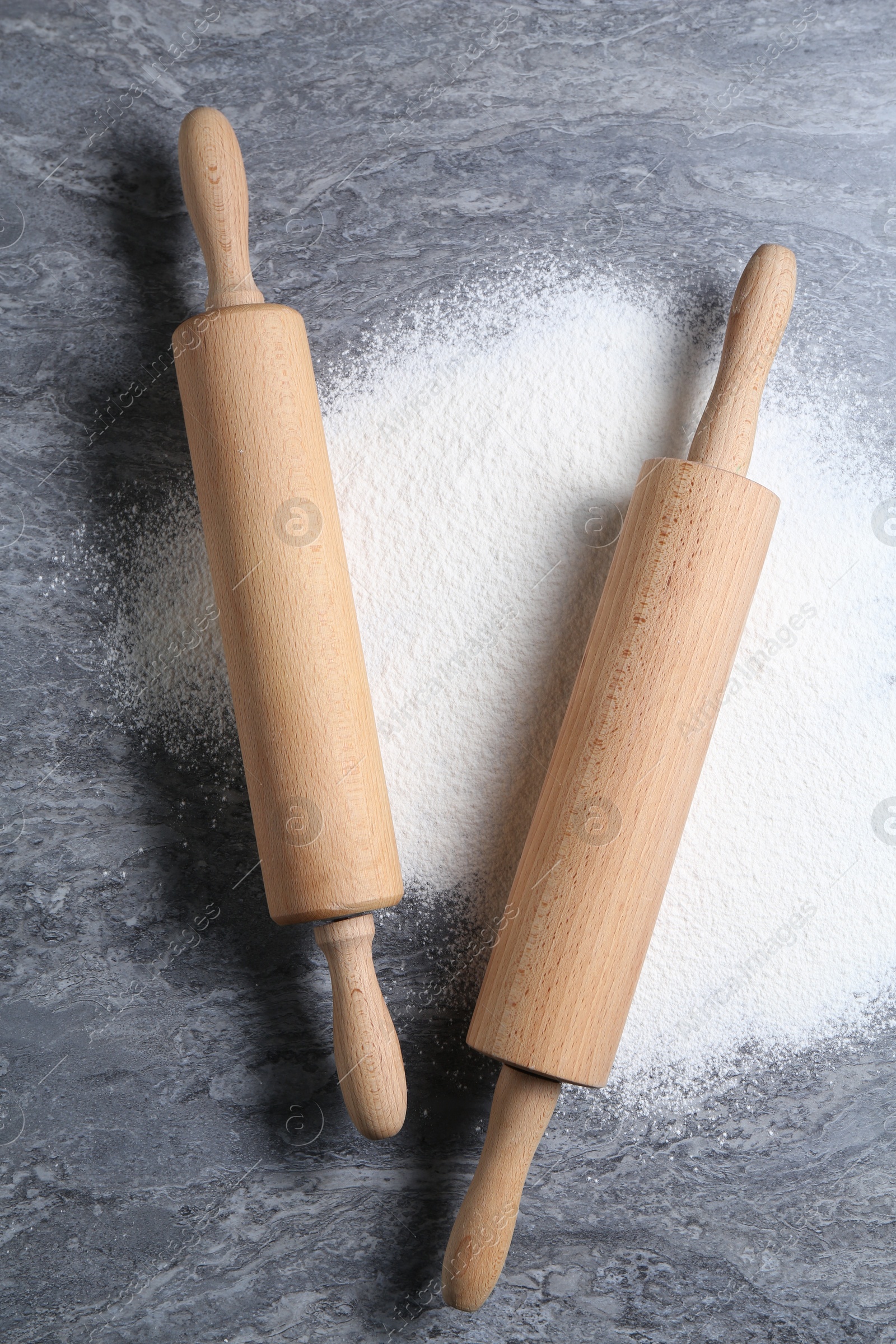 Photo of Rolling pins and flour on grey textured table, flat lay