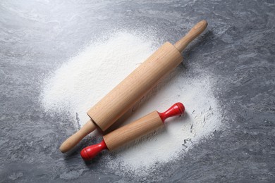 Photo of Rolling pins and flour on grey textured table, flat lay