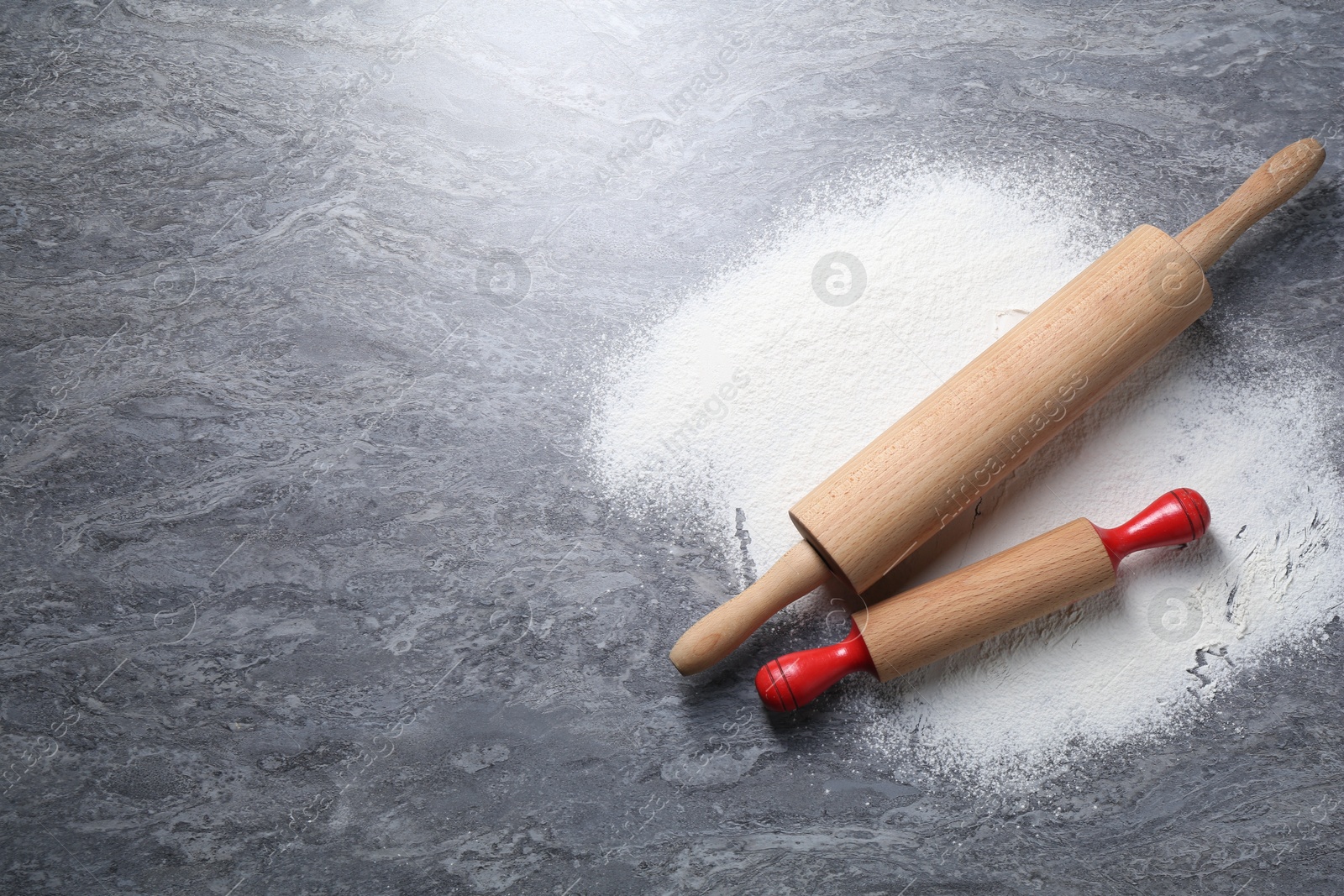 Photo of Rolling pins and flour on grey textured table, flat lay. Space for text