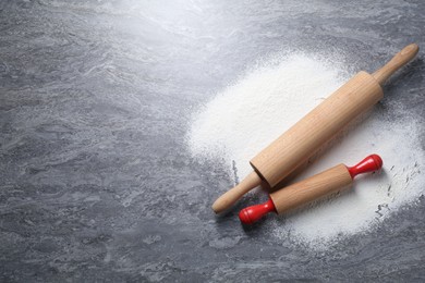 Photo of Rolling pins and flour on grey textured table, flat lay. Space for text