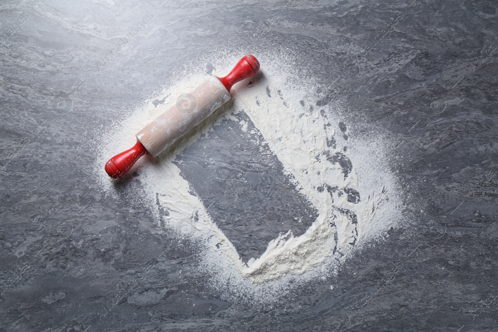 Photo of Rolling pin and flour on grey textured table, top view. Space for text