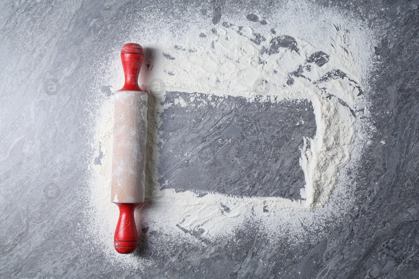 Photo of Rolling pin and flour on grey textured table, top view. Space for text