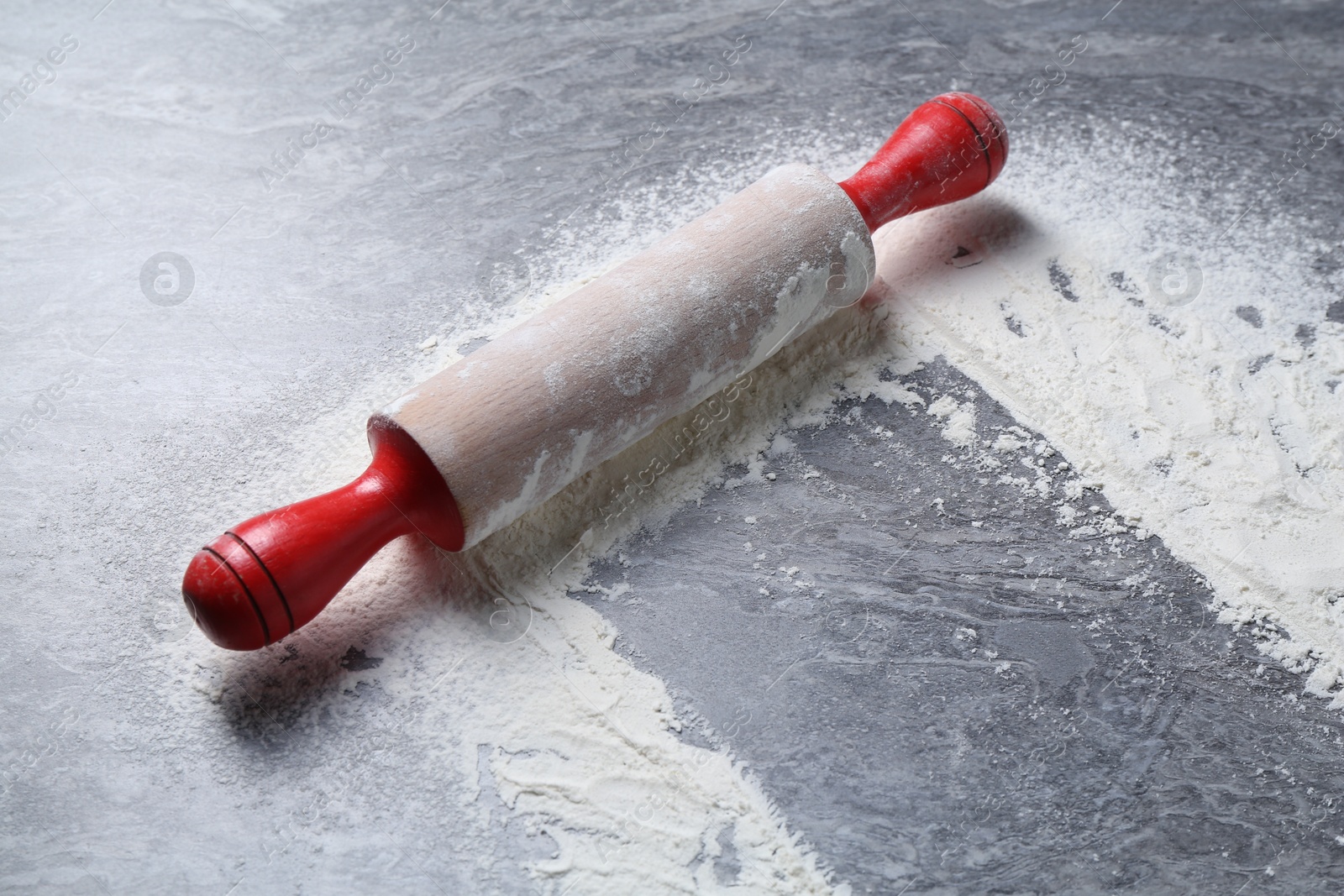 Photo of Rolling pin and flour on grey textured table, closeup