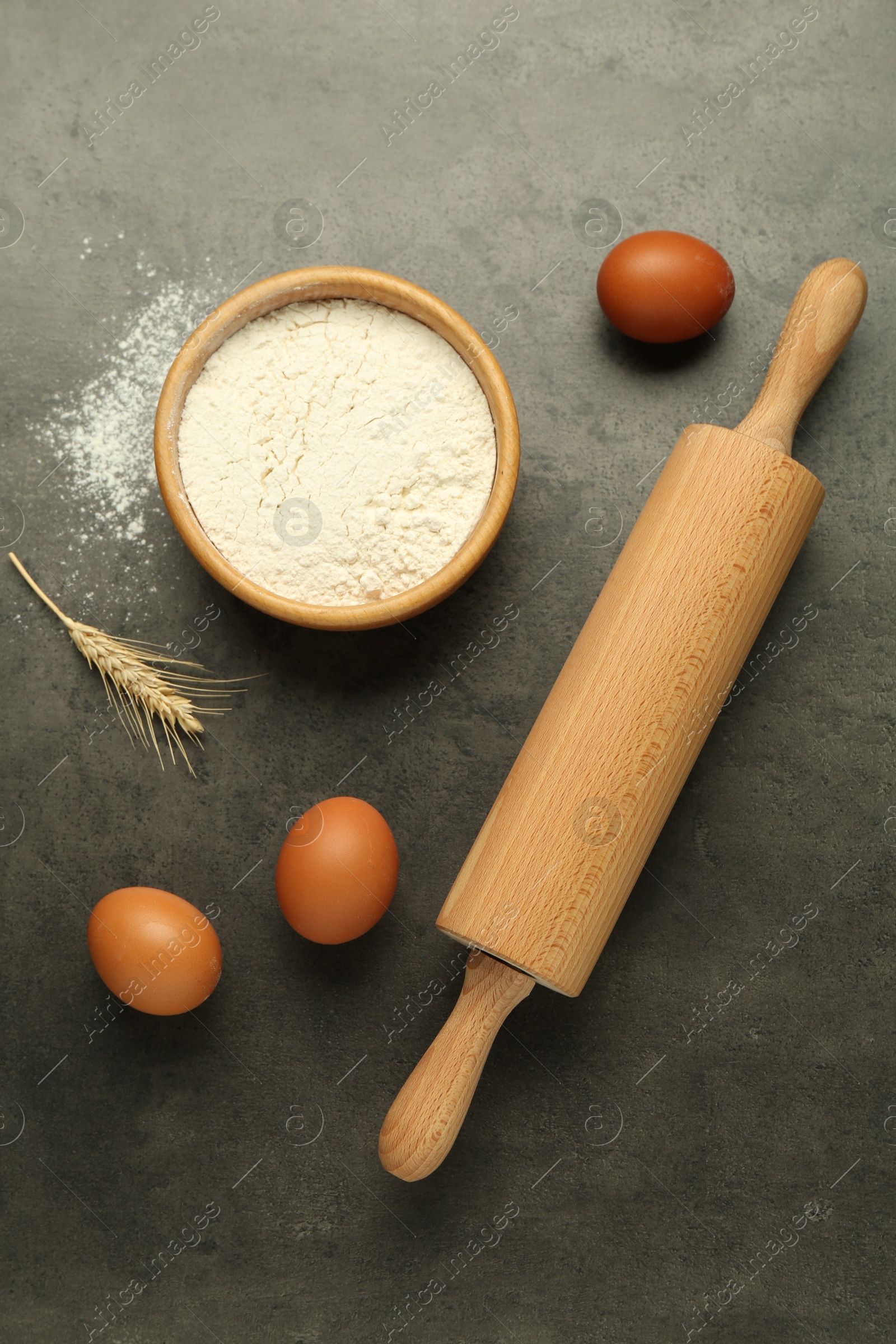 Photo of Rolling pin, bowl of flour, eggs and spike on grey table, flat lay