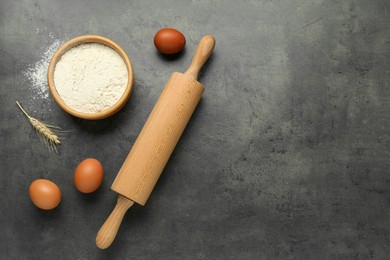 Photo of Rolling pin, bowl of flour, eggs and spike on grey table, flat lay. Space for text